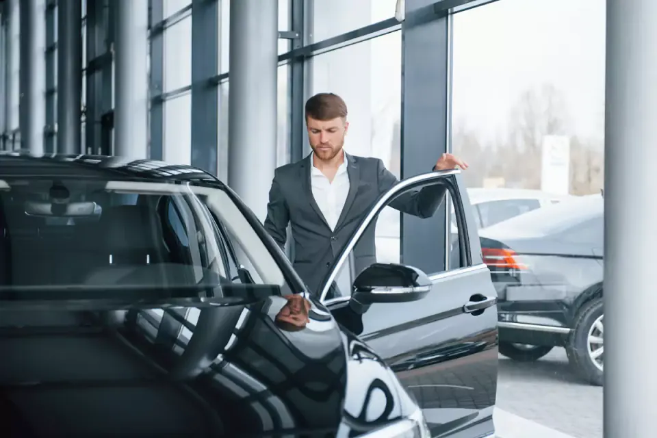 Homem de fato a abrir a porta de um carro preto num stand automóvel