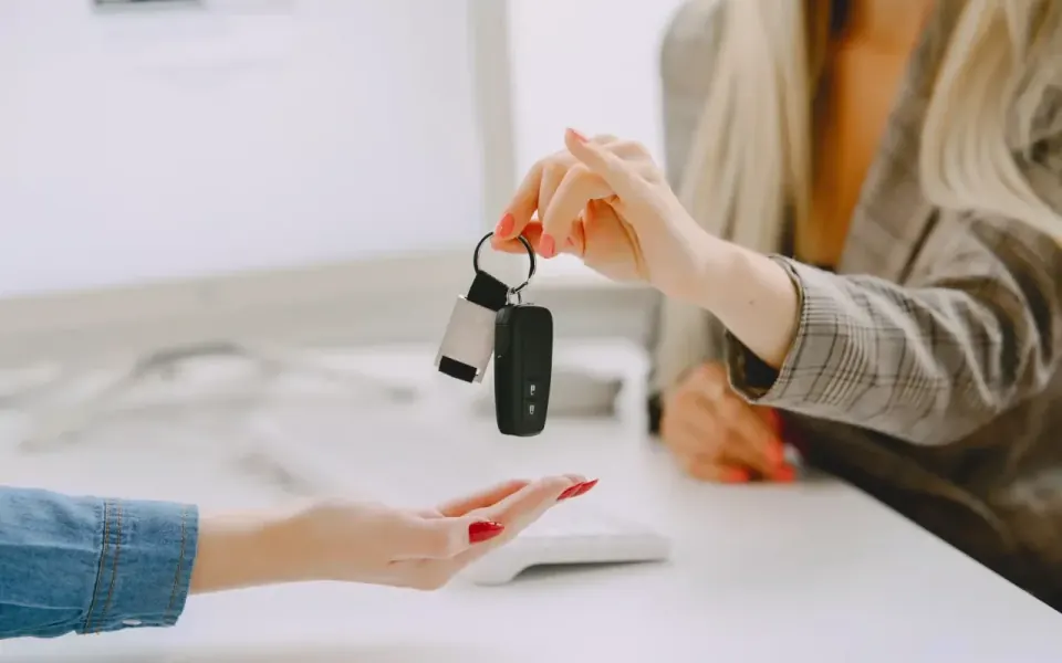 vista aproximada da mão de uma vendedora a passar a chave do carro para a sua compradora