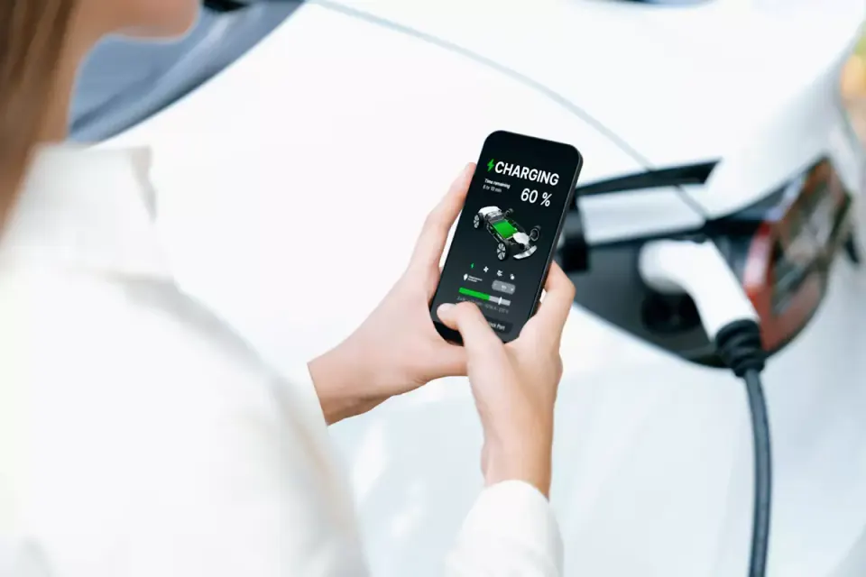 Mulher a consultar no telemóvel a carga de 60% de um híbrido plug-in ligado ao carregador