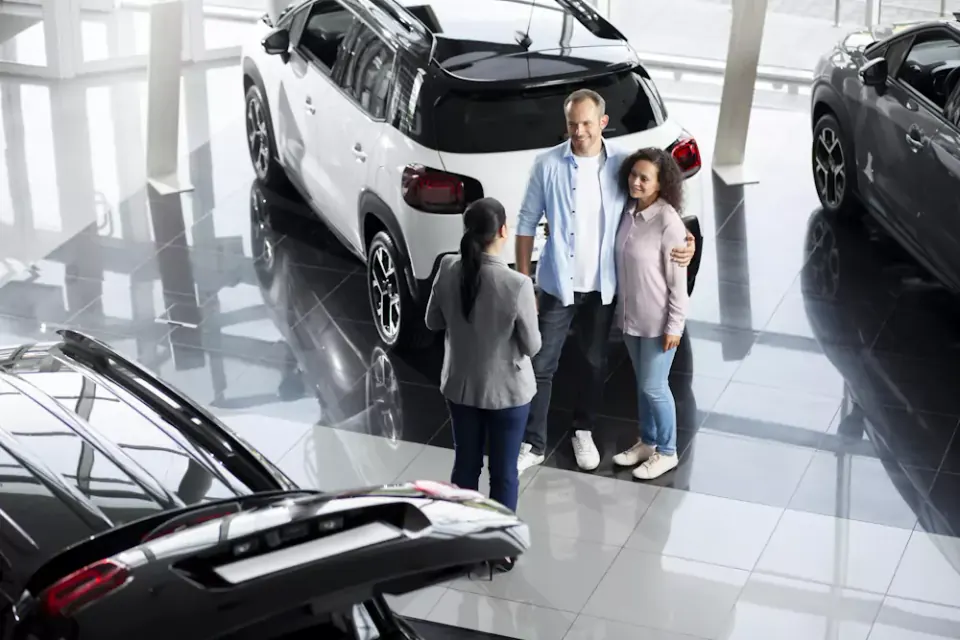 Casal a falar com uma consultora junto a um SUV branco num stand, à procura do melhor carro qualidade-preço